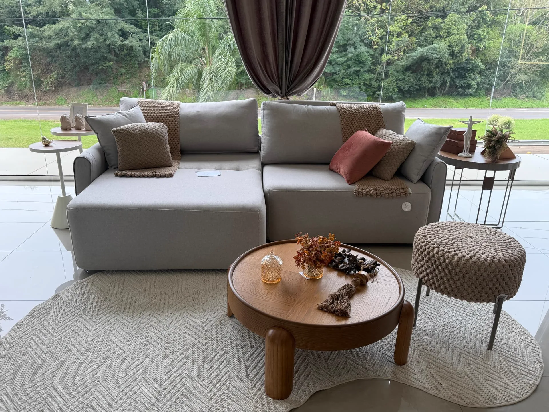 Estar do showroom com sofá claro, mesa de centro redonda e vista para o jardim
