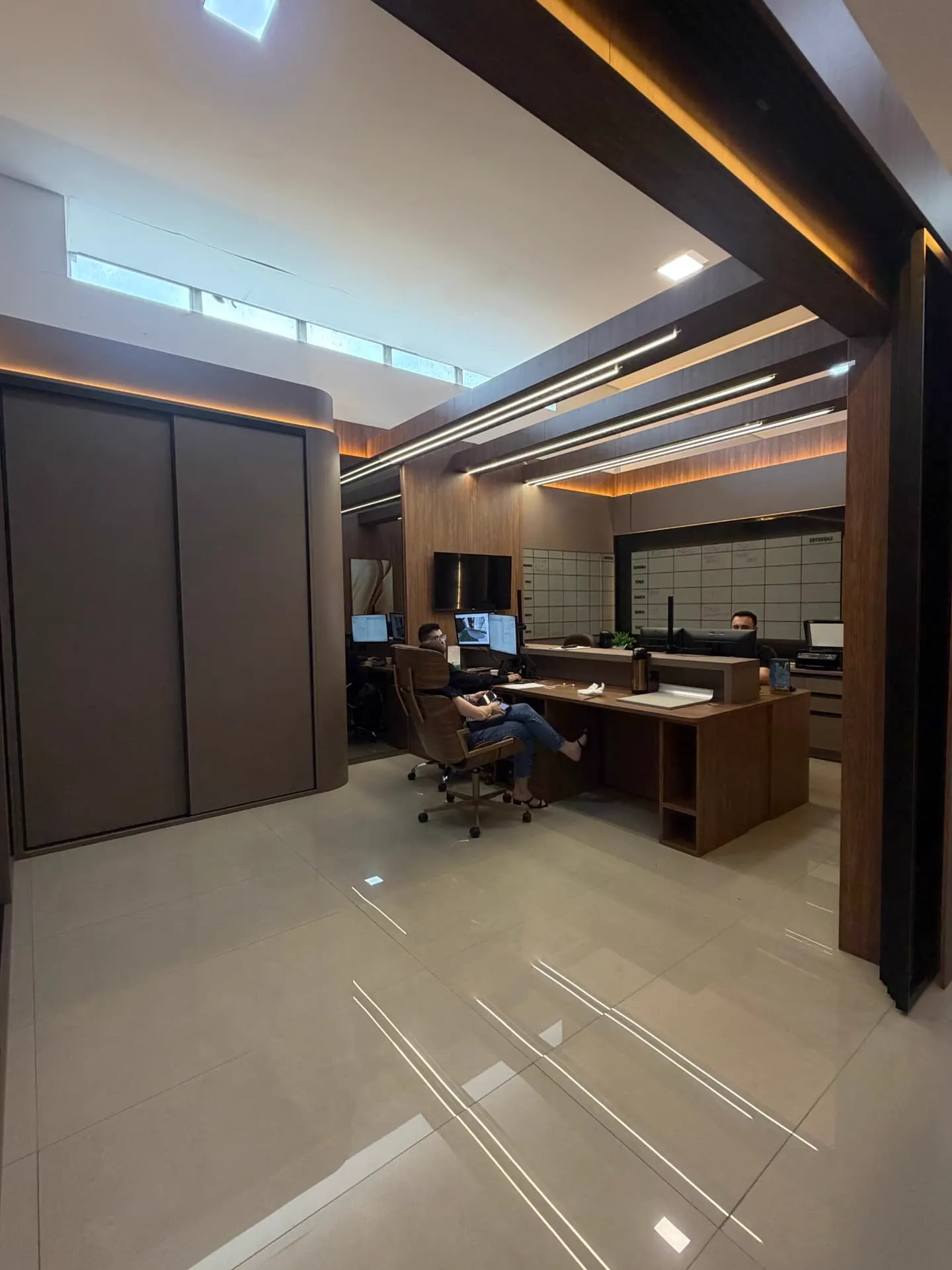 Espaço de projetos do showroom com marcenaria em madeira, iluminação linear e mesas de atendimento