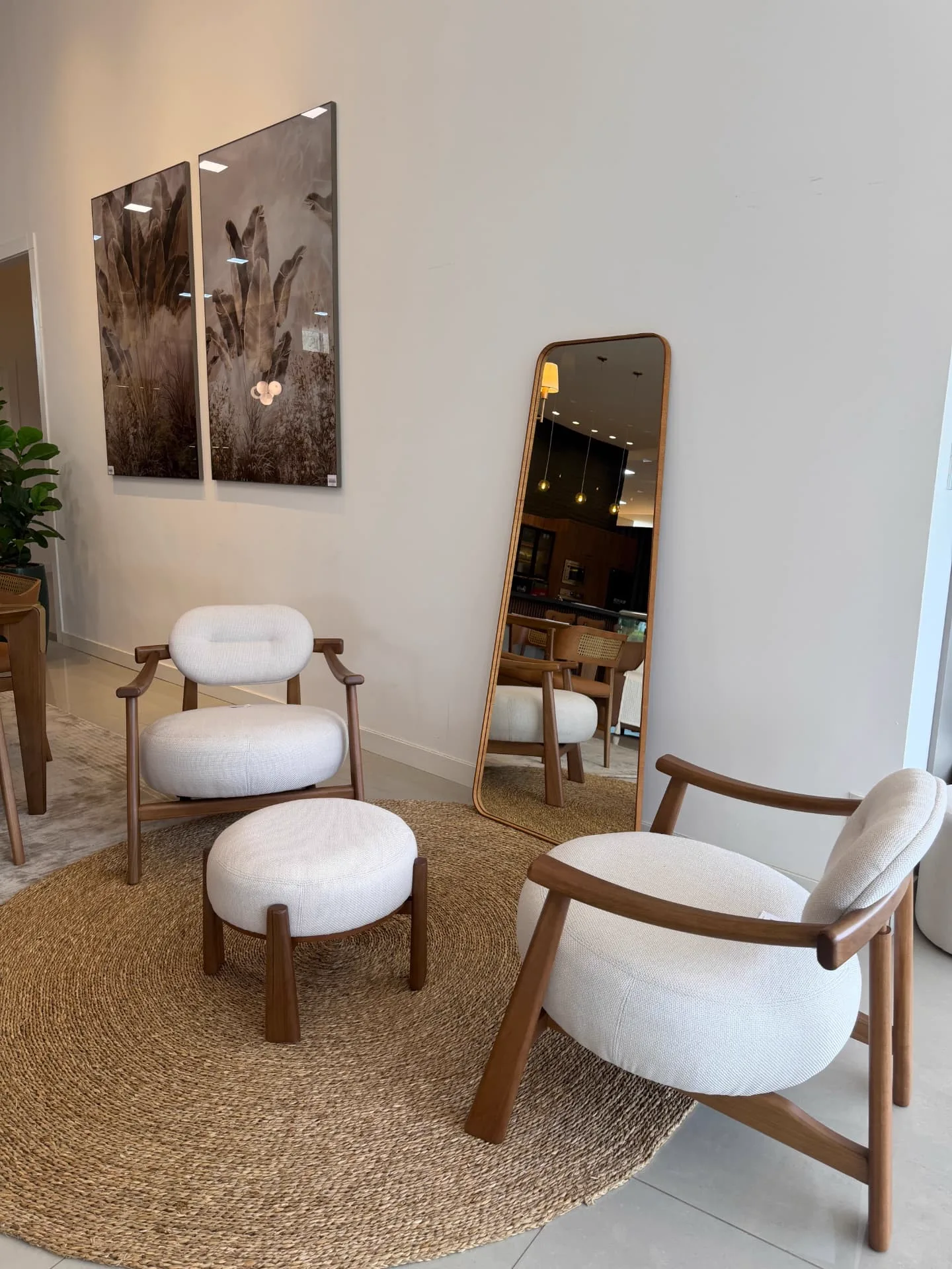 Estar do showroom com poltronas claras, espelho e tapete natural
